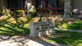 Stone sign reading 'County of Yolo Administration Center, 625 Court Street' in front of a low stone pedestal with a landscaped lawn and shrubs.